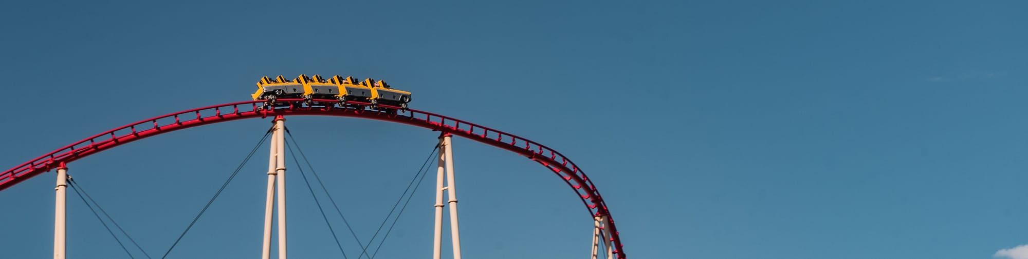 Rollercoaster cars against a blue sky, about to round a downward turn