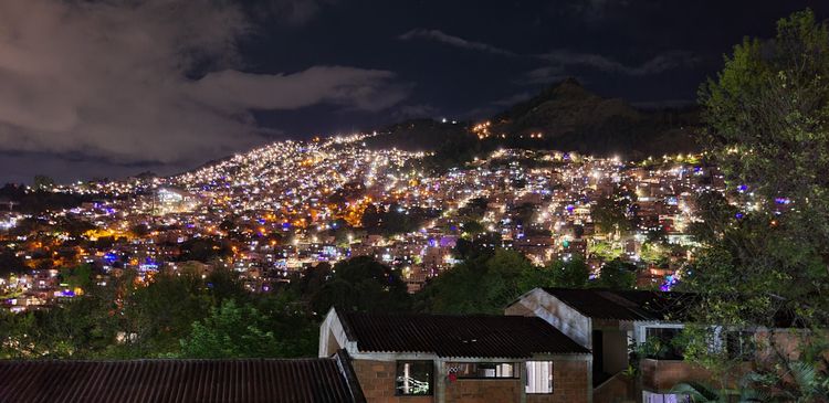 apartment buildings and trees in foreground, in background a hill covered in lights