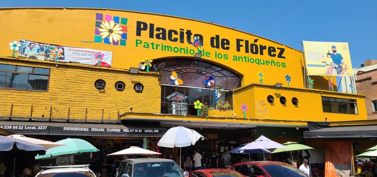 Bright yellow building painted with flowers, says "Placita de Florez: Patrimonio de los antiquenos"