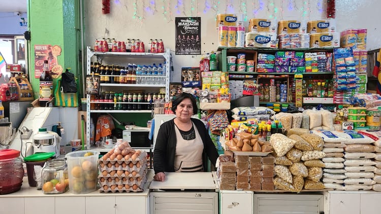 Ecuadorian woman in black and tan surrounded by many products from toliet paper to eggs.